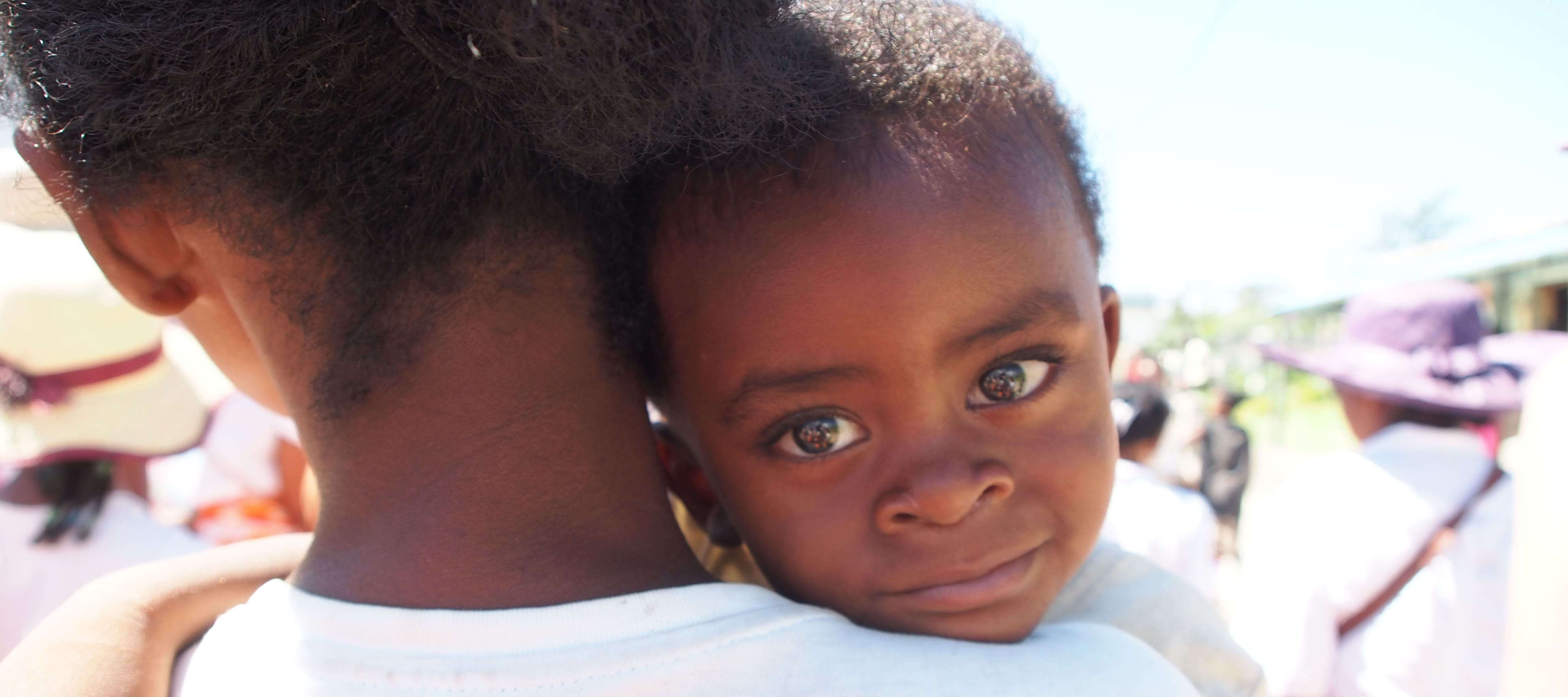 A baby looks over their mother's shoulder