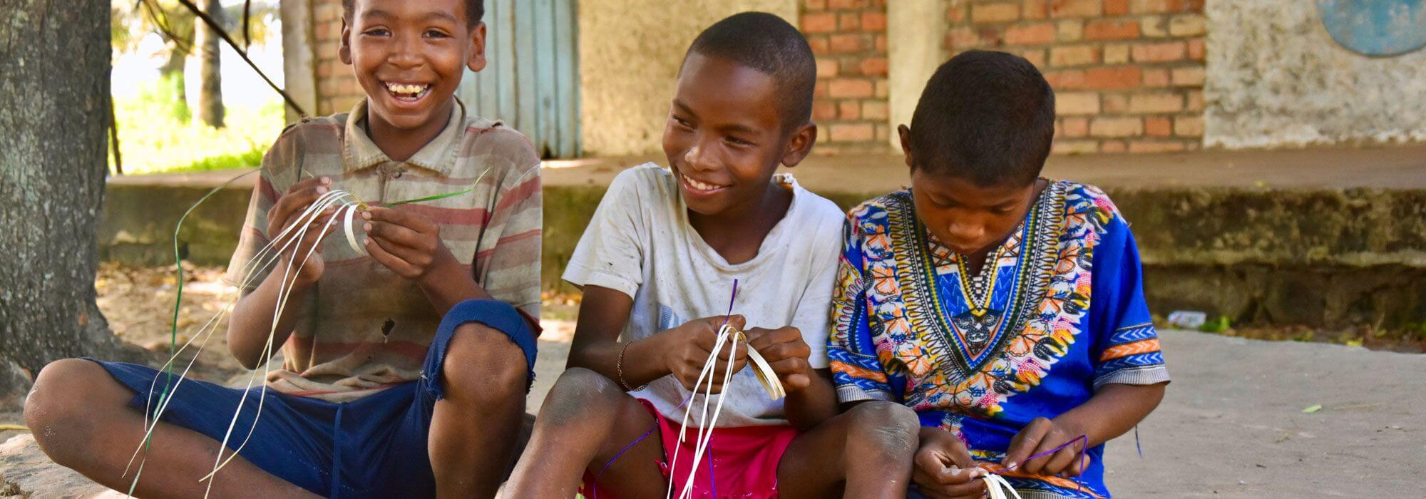 Three smiling kids learning to weave mahampy bracelets