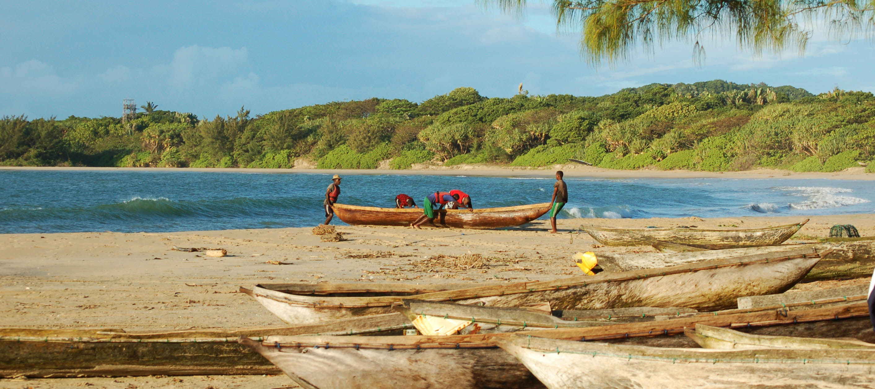 Fishermen push a wooden pirogue into the sea