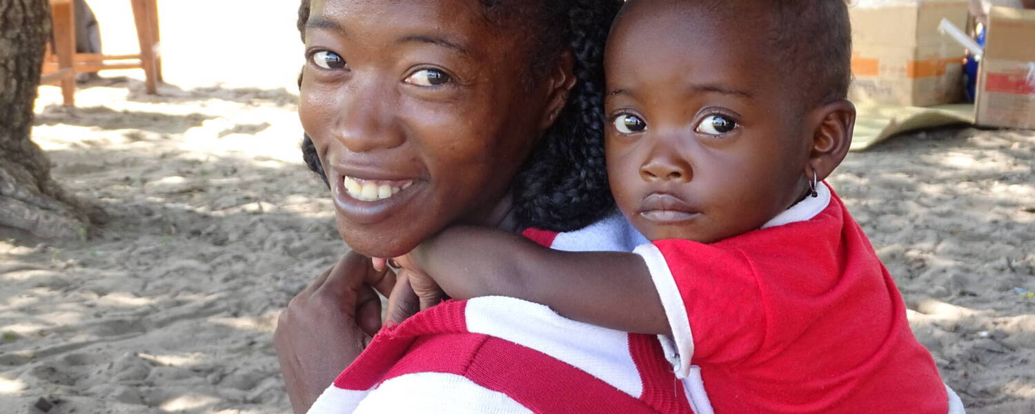 A mother smiles with a child on her back